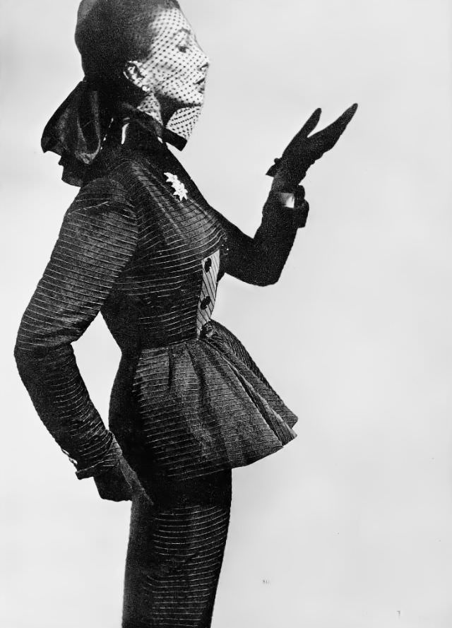 #20 Barbara Goalen in elegant suit of black ottoman silk with a raised horizontal rib and a front-flaring basque on the long jacket by Lachasse, worn with silk spotted veil, 1951.