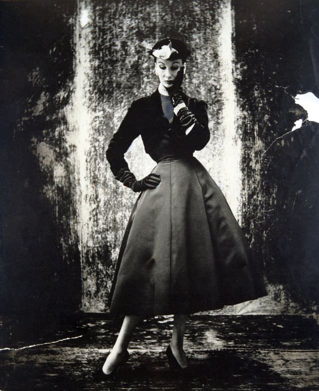 #26 Barbara Goalen in short black velvet jacket over faille dress with bell skirt by Marcus at Harvey Nichols, 1951.
