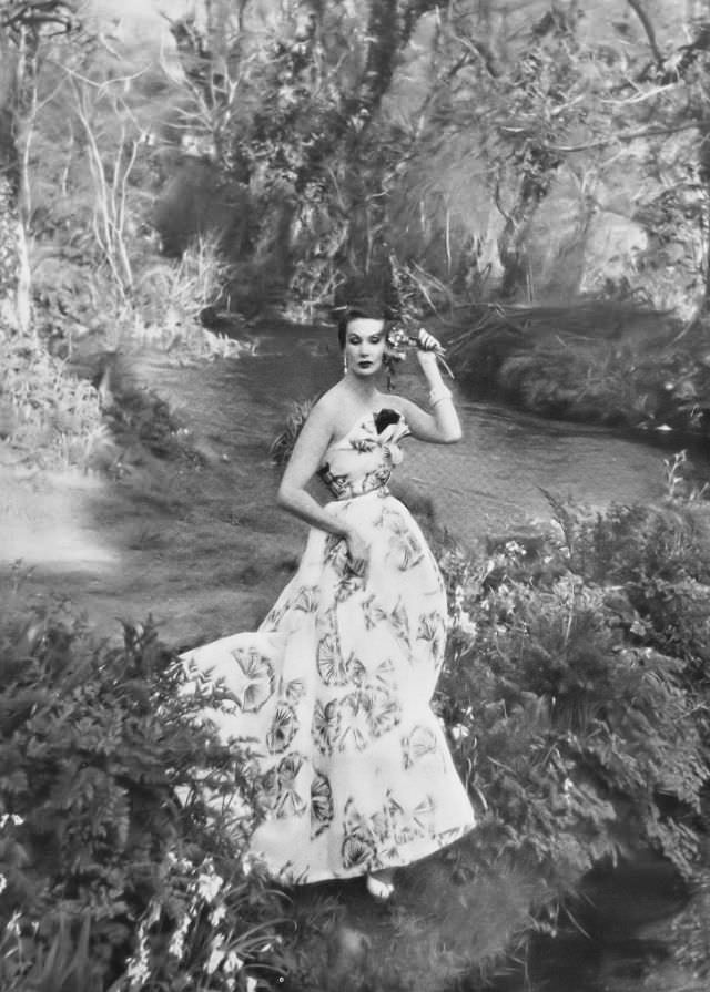 #32 Barbara Goalen in romantic evening dress in white organdie patterned with black and gold dandelions, the bodice fans out, offset by one red rose, from Worth’s Boutique, 1952.
