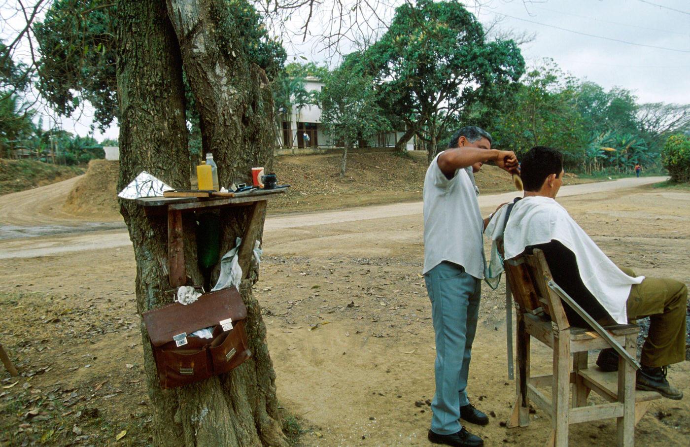 #49 Cuban man combing a Cuban boy’s hair beside a tree trunk, Cuba, 1990.