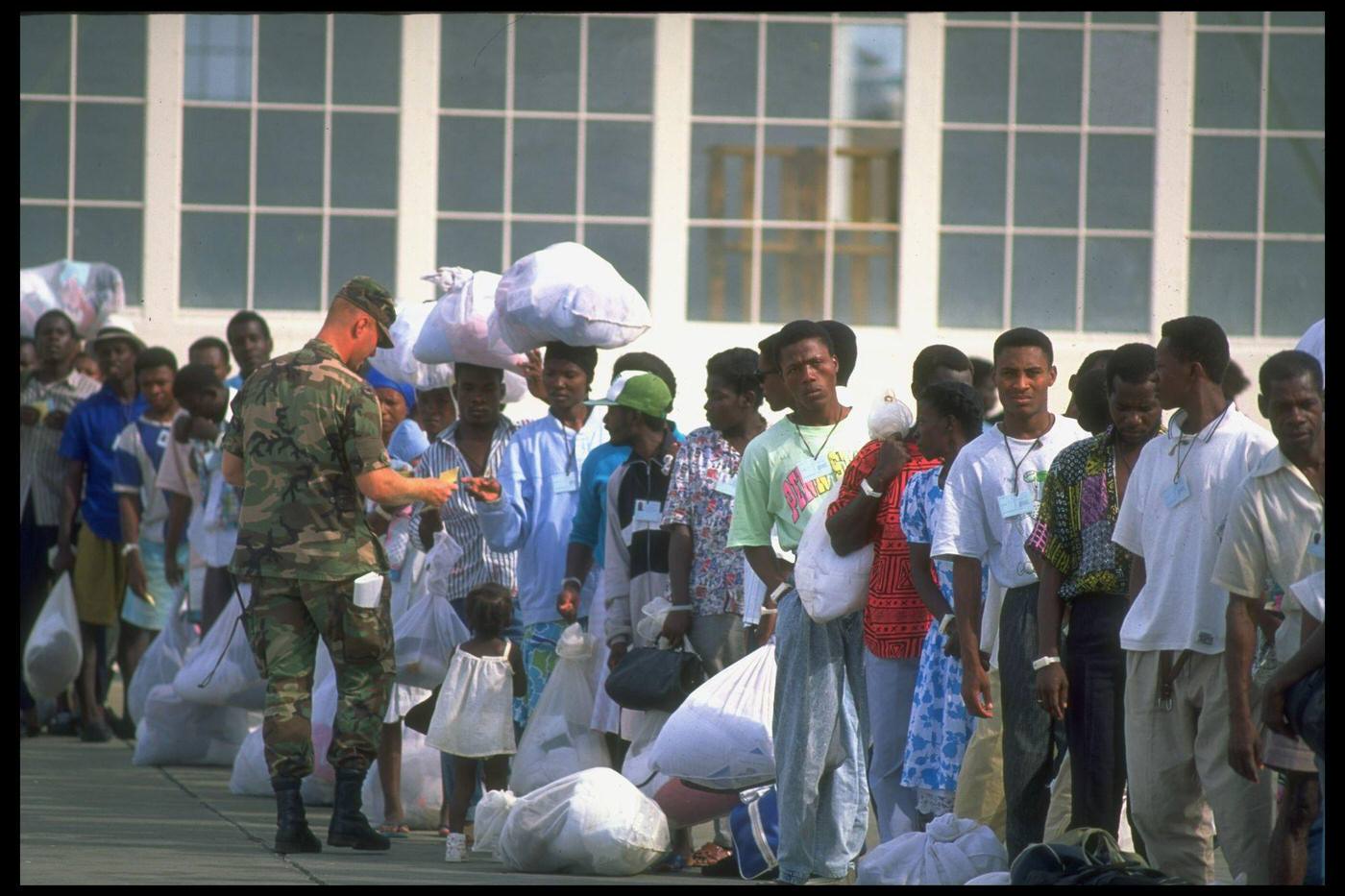 #74 Haitian refugees picked up at sea by the Coast Guard lining up for processing at a US naval base camp, facing deportation/repatriation.