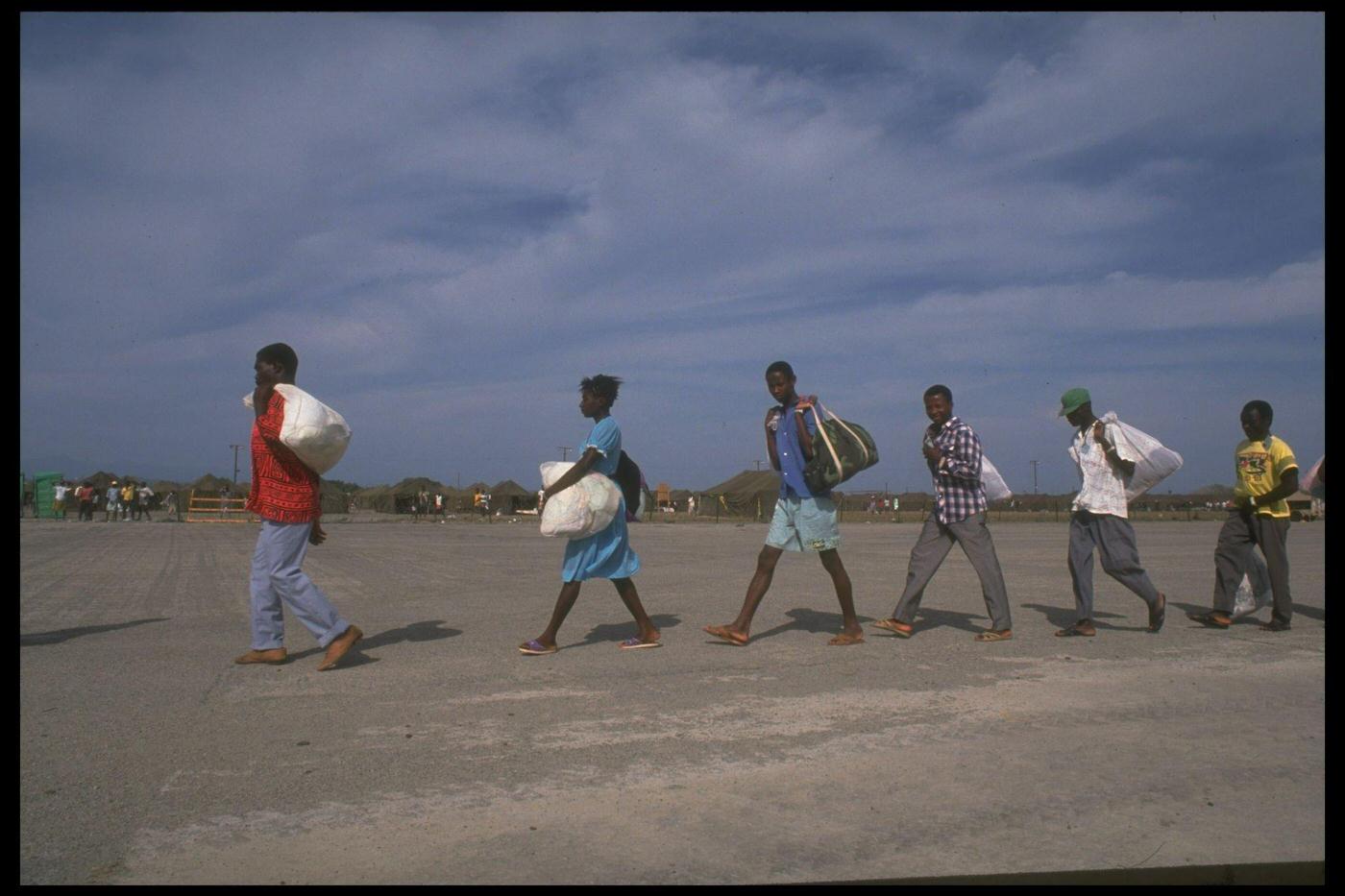 #75 Haitian refugees picked up at sea by the Coast Guard arriving/leaving at a US naval base camp, facing deportation/repatriation.