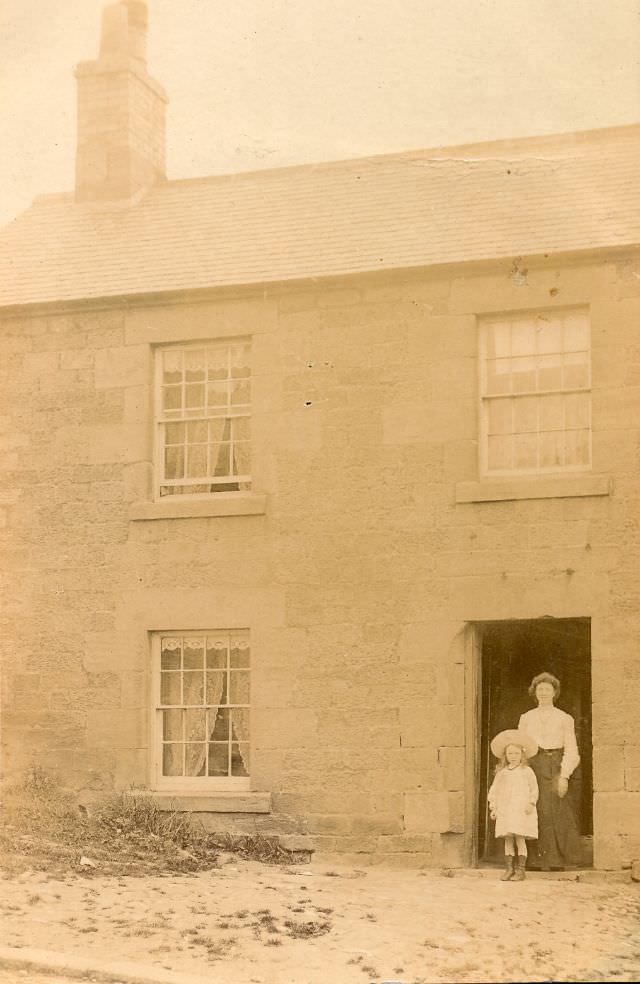 #29 Mother and child stand in doorway of stone-built terrace house