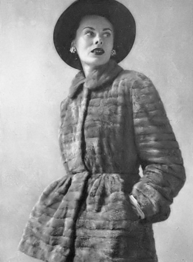 #20 Meg Mundy in ermine tunic, its waist is tight and peplum wide, by Maximilian, midnight-blue beaver hat by Lilly Daché, Harper’s Bazaar, 1947.