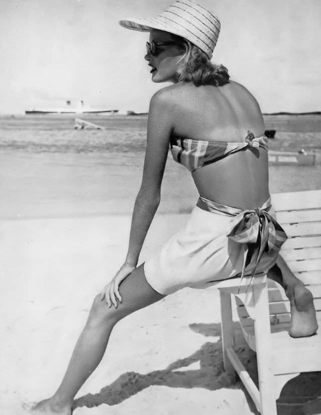 #37 Model in cotton halter top, plaided in yellow, black and brown with plain shorts of yellow sharkskin, tied with plaid sash, by Cabana Sportswear, Montagu Beach, Nassau, Bahamas, Harper’s Bazaar, 1948.