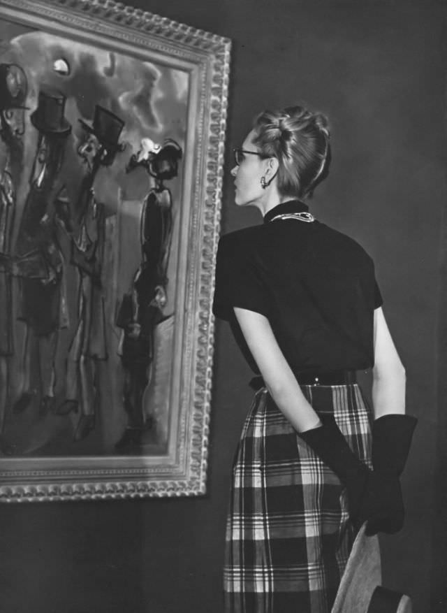 #4 Model in a bright-and-black gingham dress with bold plaid skirt and short sleeves, belted in black patent leather by David Crystal, in front of a painting by Max Weber, Vogue, 1945.
