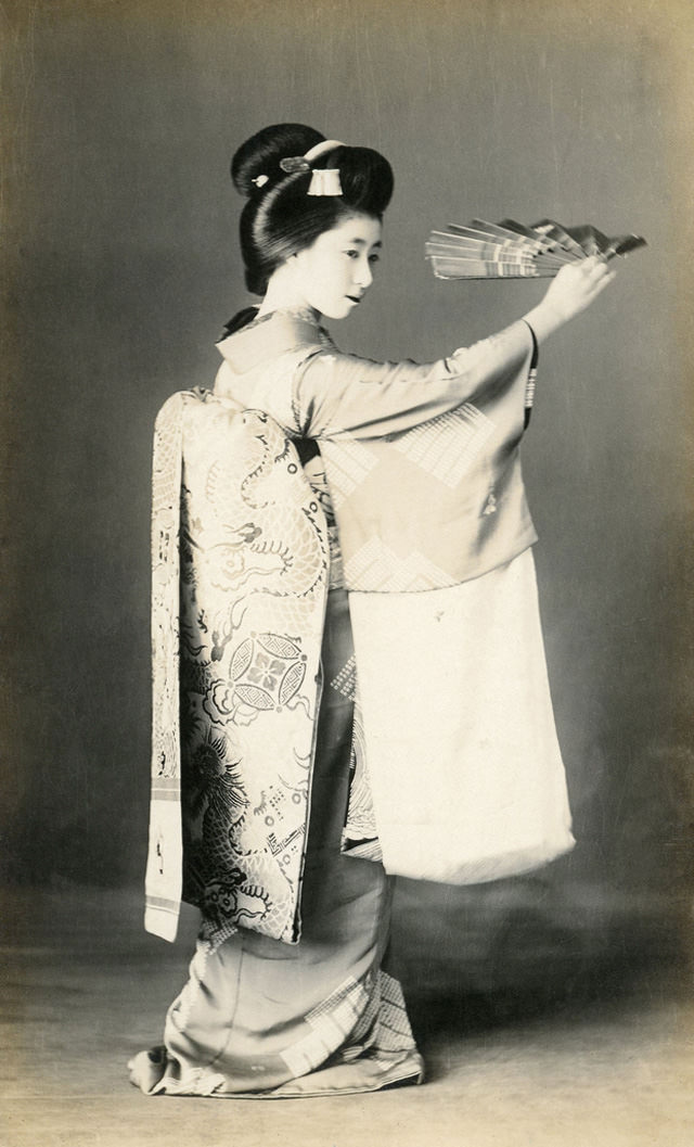 #15 Maiko dancing with a mai-ogi (dancing fan), her obi (sash) decorated with dragons and pearls, 1910s