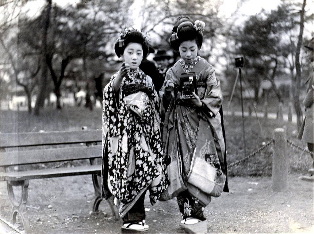 #5 A Maiko girl taking a photograph with an early Kodak folding camera, while being guided by another Maiko, 1920s