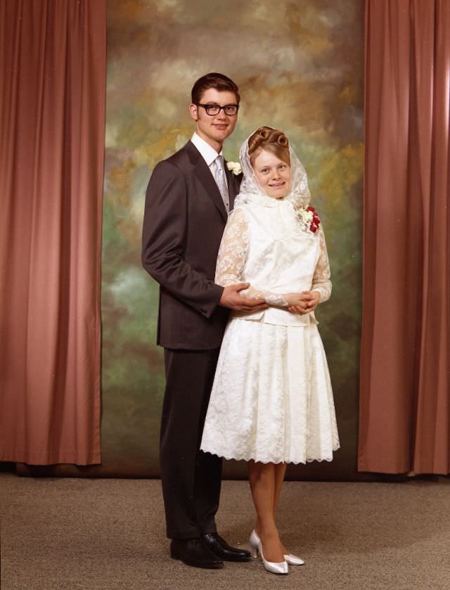 #11 Wedding portrait of a Doukhobor couple. The groom is wearing a brown suit, with a white shirt and silver tie. The bride is wearing a knee-length white dress, a corsage, and a traditional white headscarf, May 8, 1971