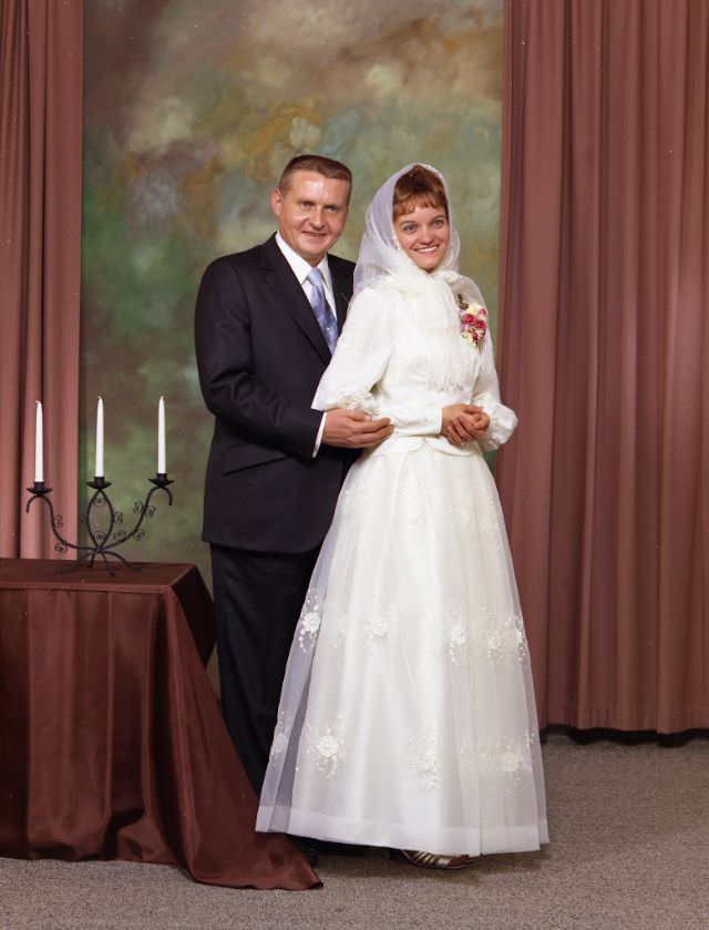#12 Wedding portrait of a Doukhobor couple. The groom is wearing a dark suit, with a white shirt and blue tie. The bride is wearing a white dress, a corsage, and a traditional white headscarf, November 27, 1971
