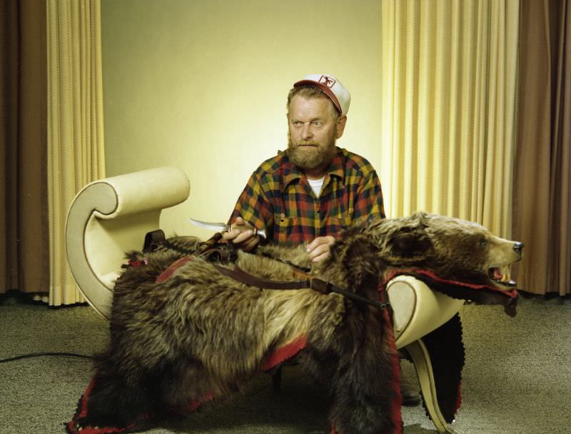 #31 Portrait of a man with a bear hide and hunting paraphernalia. He is wearing a cap and plaid button-up shirt, June 3, 1978