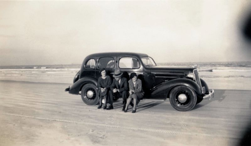 #14 Two ladies and a fellow with a fedora hat posing on the running board of a 1935 Chevrolet Master DeLuxe Sedan in late afternoon sunshine, 1936