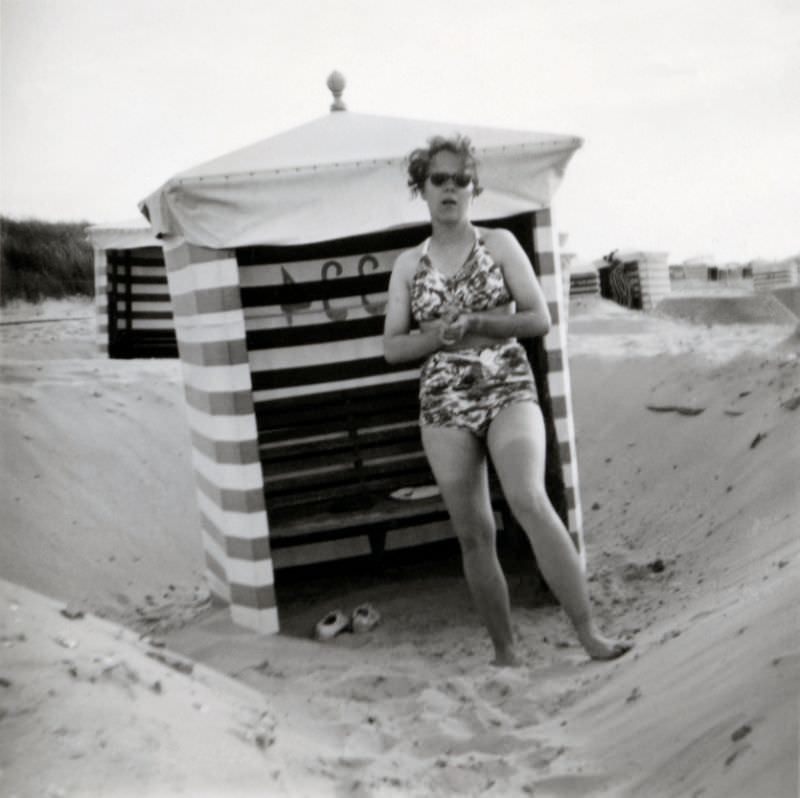 #16 A bashful young lady in a two-piece swimsuit posing on a beach.