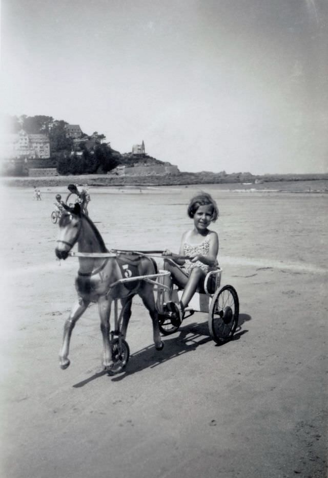 #26 A blonde girl posing in the seat of a pedal tricycle on a beach in midday sunshine.