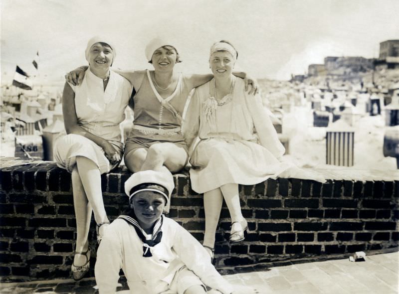#3 Three fashionable ladies and a freckled boy in a sailor suit posing at the seaside. In the background, the breach is covered with typical German beach chairs (Strandkörbe), 1928