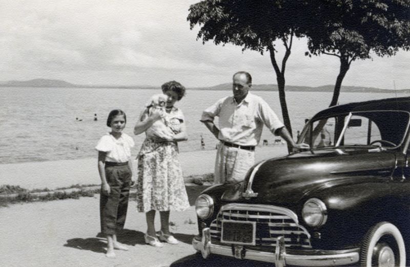 #30 Three members of a middle-class family posing with a Morris Oxford in bright midday sunshine at the seaside, 1955