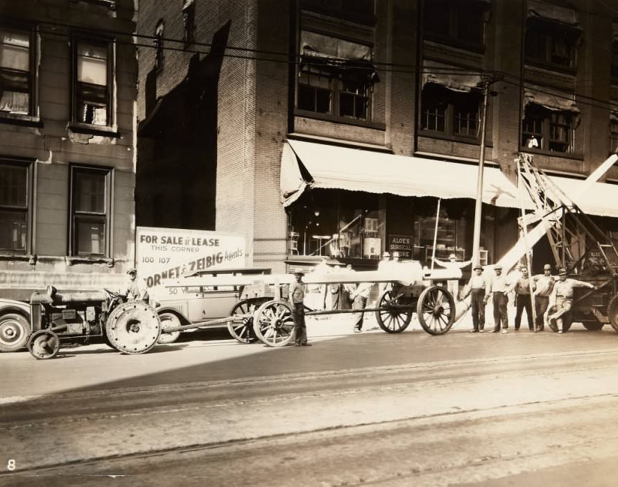 #138 Workmen posing next to the posts they are installing for street lights on the 1800 block of Olive Street in 1920. The storefront for Aloe’s Surgical Store can be seen behind them.