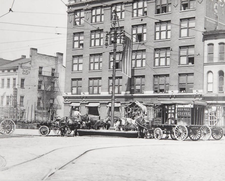 #155 Numerous teams of horse-drawn carriages resting at a watering trough in front of the Kroger Ames James Grocer Co. building at Third Street and Washington in 1920
