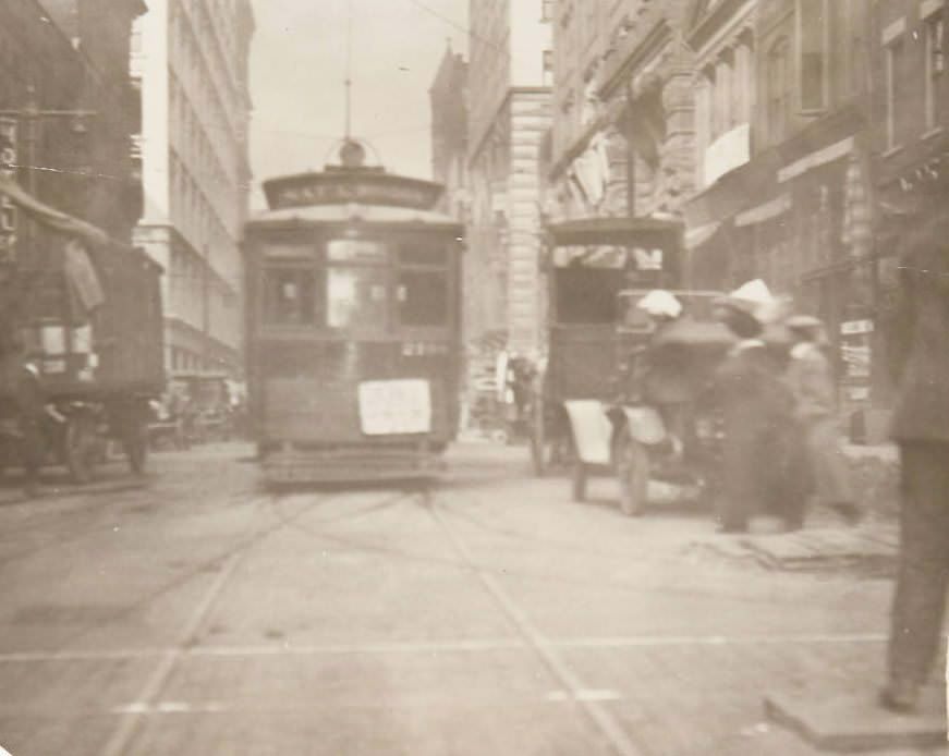 #92 Daily streetscene of downtown St. Louis, likely on Pine Street, with a street trolley and automobiles visible, 1920