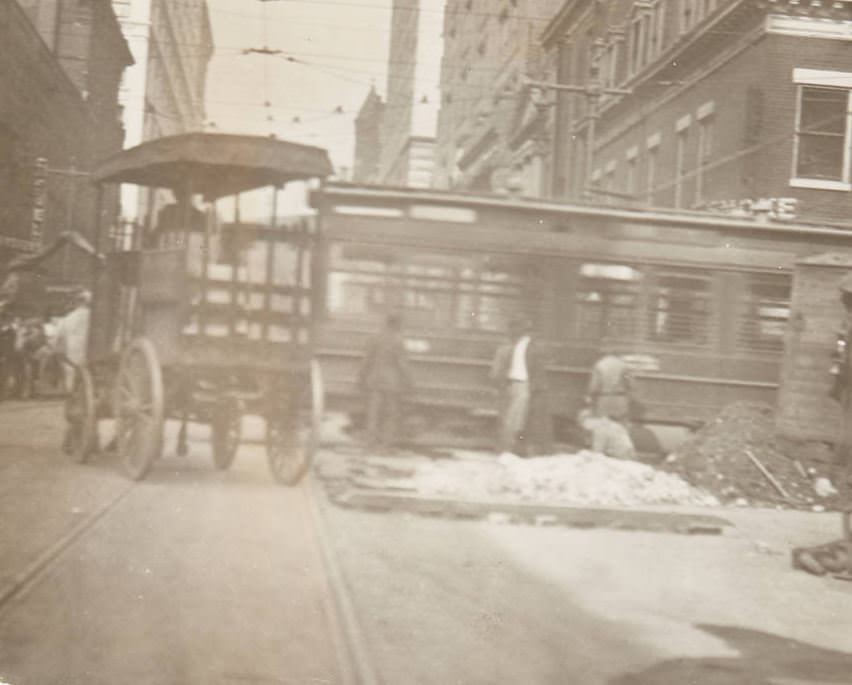 #106 Street repairmen at work, likely near Pine Street downtown with a street trolley in the background and a work cart laden with bricks parked next to the repair site, 1920