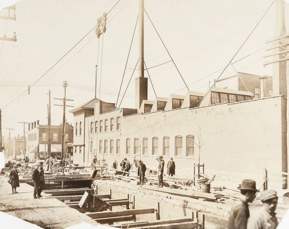 #136 Road construction projectin 1920. Workmen use a cable pulley system to lower a large metal container into an underground shaft.