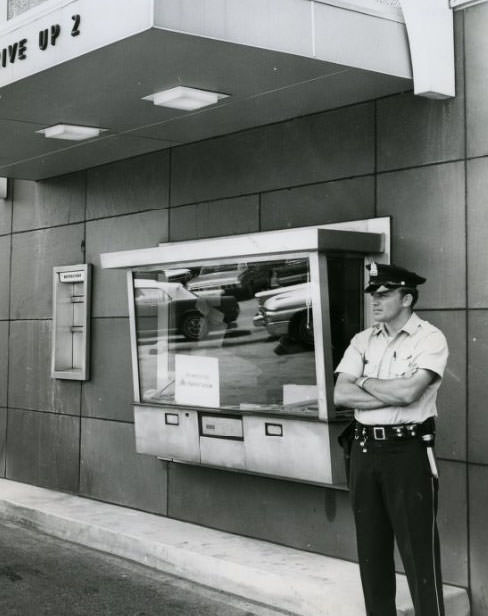 #59 Patrolman stands guard at walk up window of the Gateway Bank, 3412 Union where two holdup men held Peggy Squires, bank teller, 1960