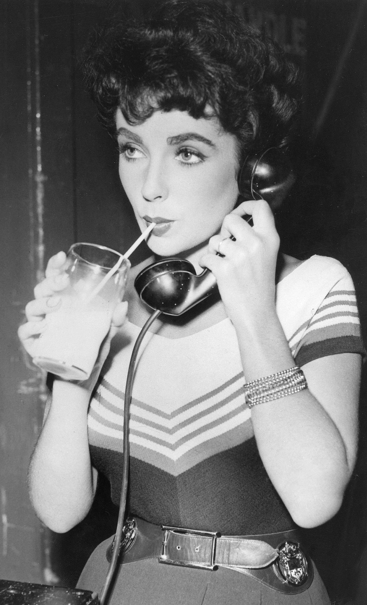 Elizabeth Taylor with a phone and milk glass during the filming of ‘Girl Who Had Everything’ (1953), USA.