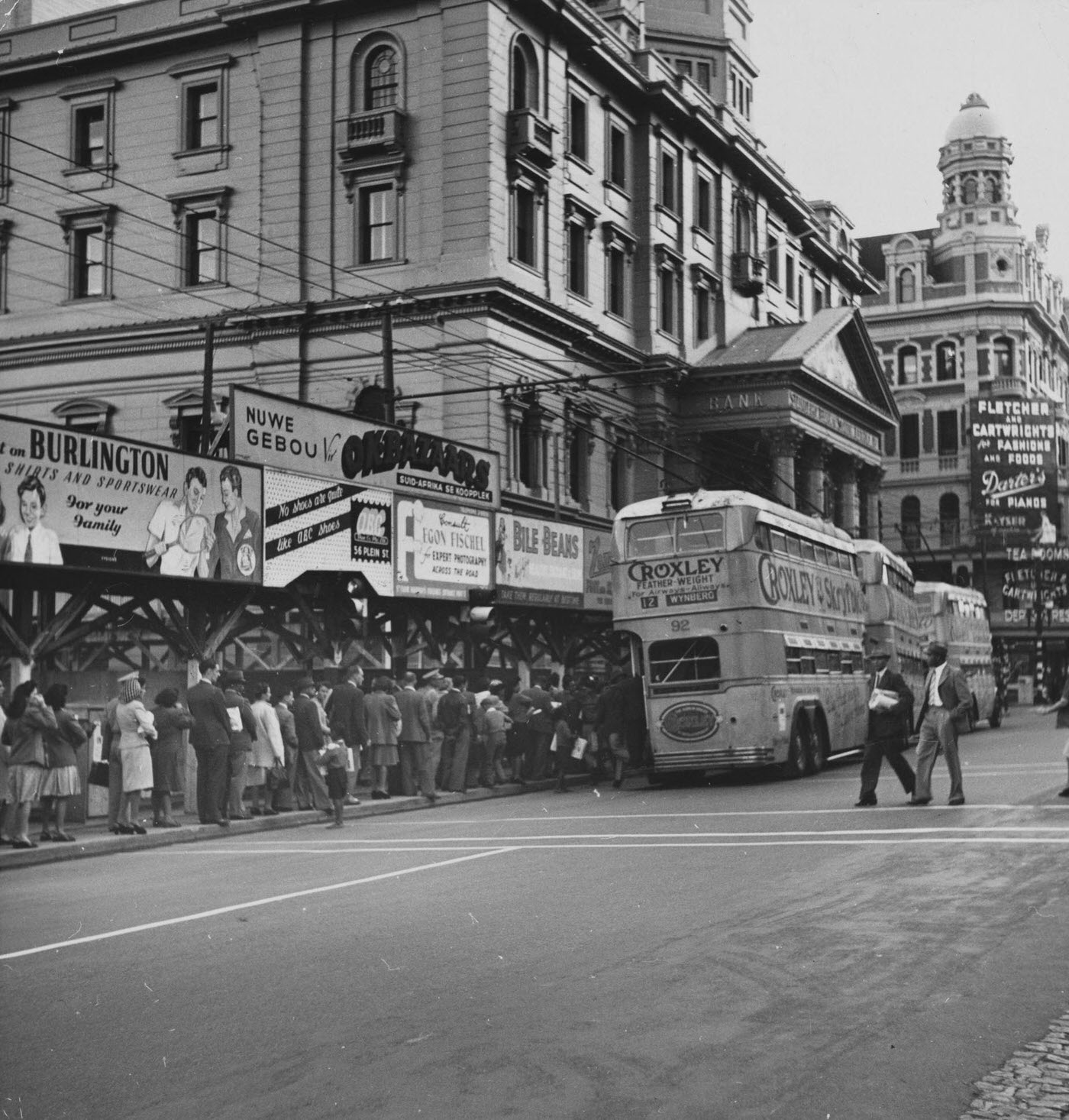 #80 People slowly file onto a double-decker bus parked outside a bank, in Adderley Street.