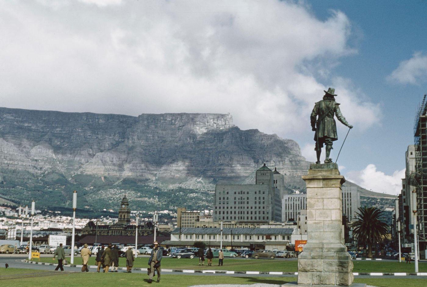 #85 Pedestrians walk past the statue of Jan van Riebeeck at the end of Adderley Street, with Table Mountain in the background, in the center of the city of Cape Town, 1960