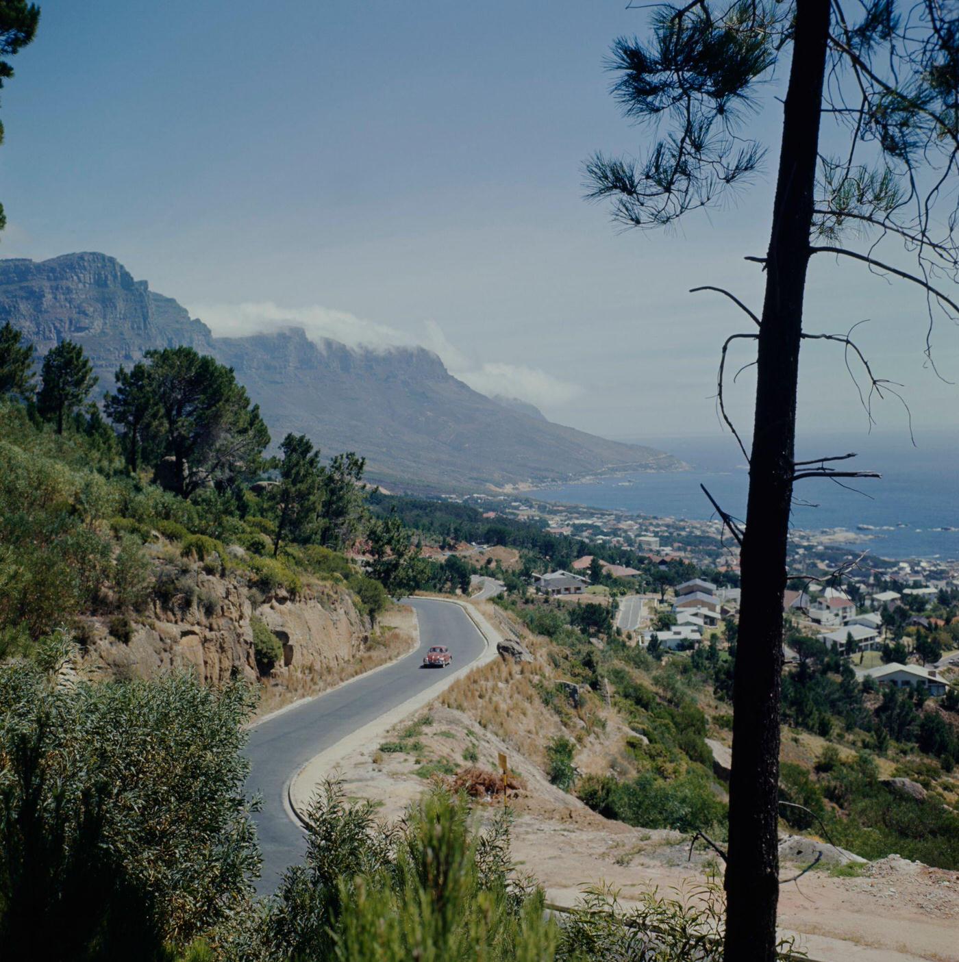 #94 A car drives along a road above Camps Bay, a suburb of Cape Town overlooking the Atlantic Ocean, 1966