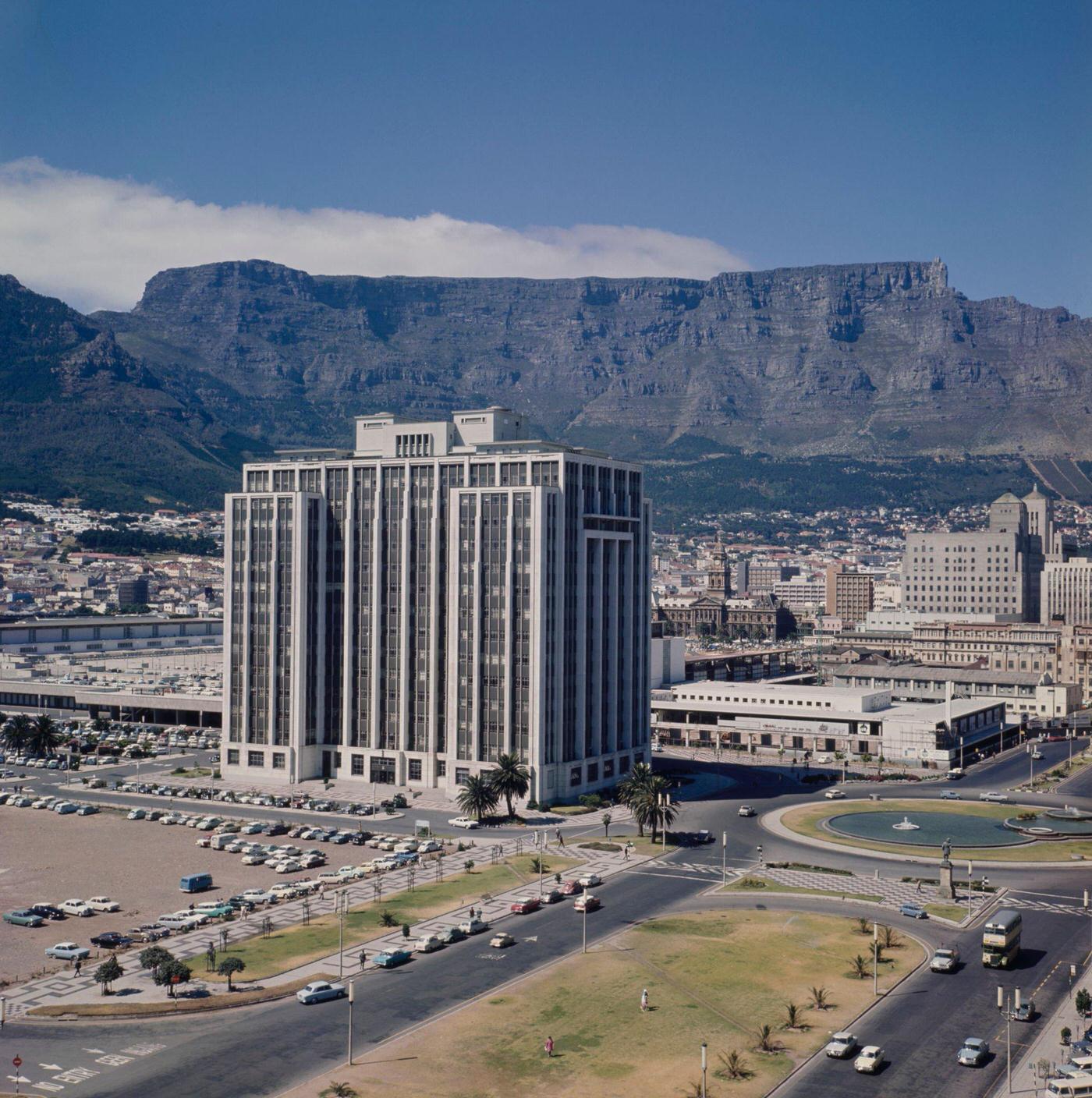 #95 Traffic drives past the Adderley Street Fountain and down Heerengracht Street in the Foreshore Place district of the city of Cape Town, 1960