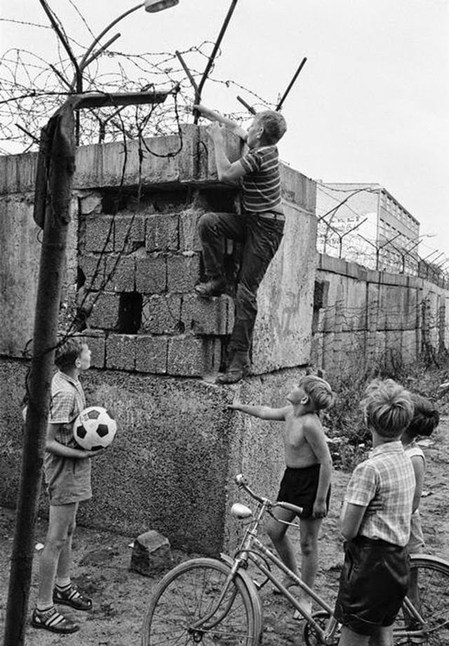 #6 Scene at the Berlin Wall near Bernauer Strasse. Four children, one of them with a soccer ball and another with a bike, watching a fifth child climbing up the Wall.