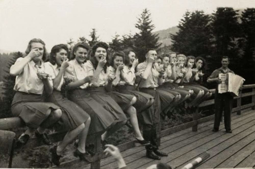 #2 Twelve SS auxiliaries sit happily on a fence railing eating blueberries given to them by an SS officer.