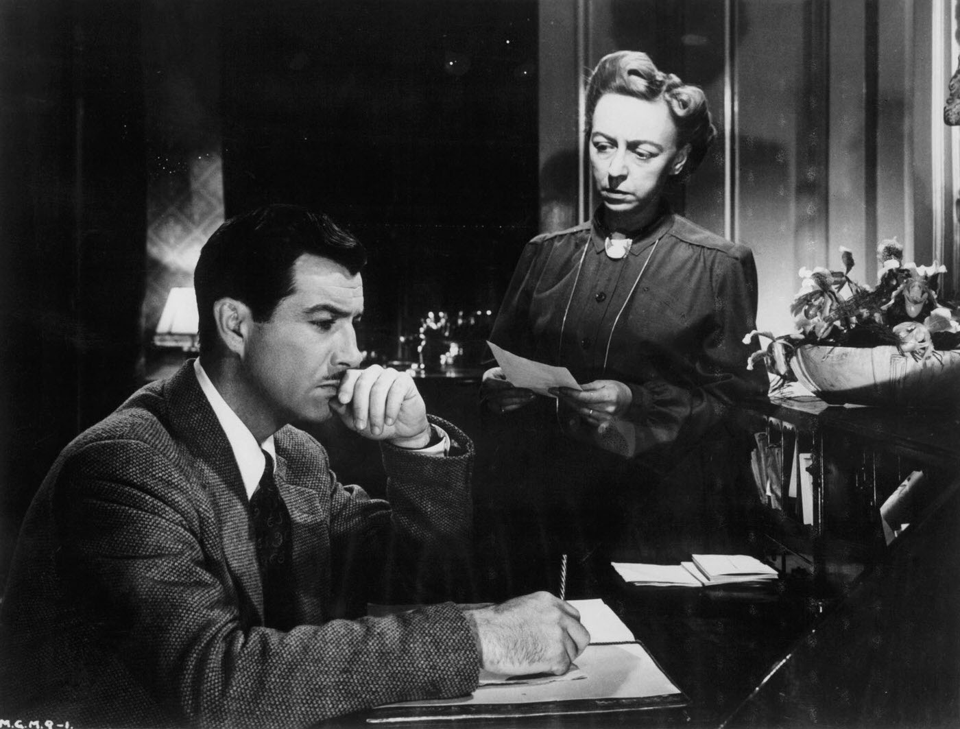 Robert Taylor writing as an unidentified woman looks at him in a scene from the film ‘Conspirator’, 1949.