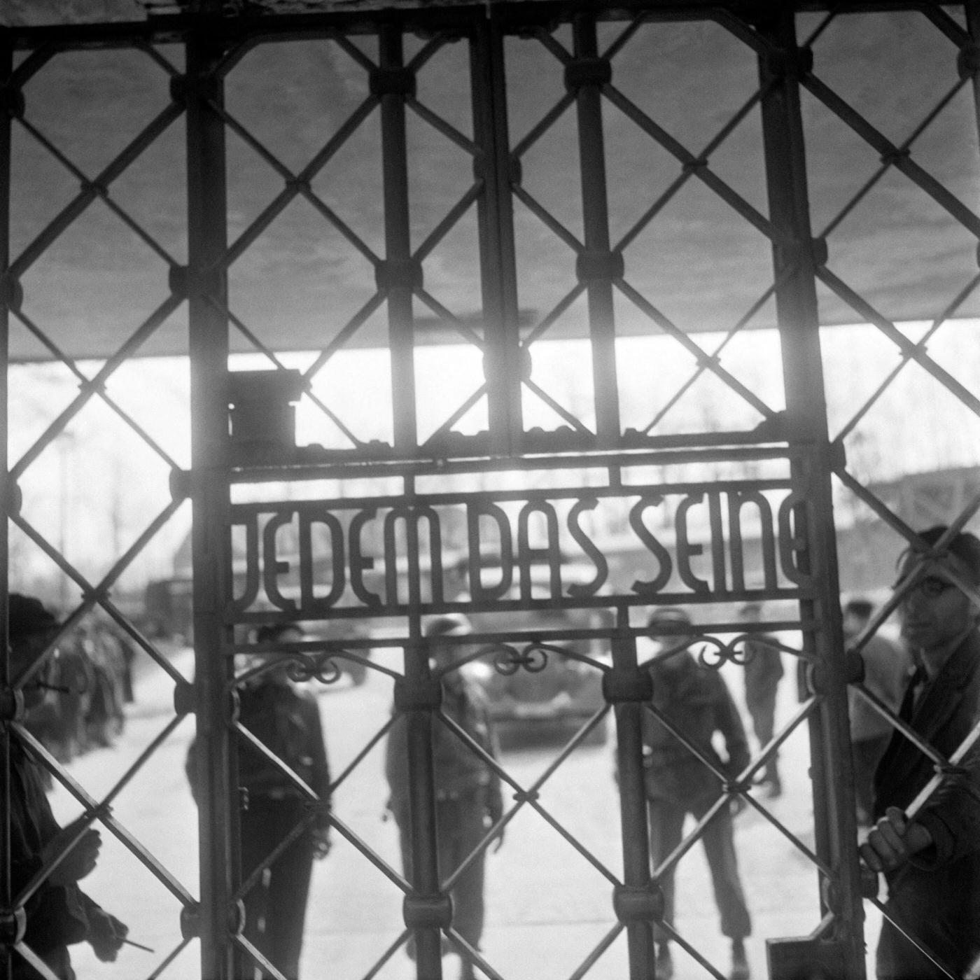 #15 Prisoners and US army soldiers stand behind the gate of Buchenwald concentration camp with the inscription “Jedem das seine” (to each his own), April 1945.