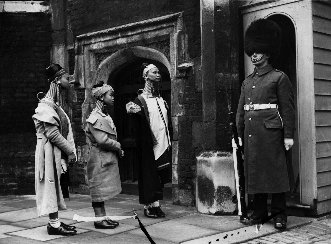 #9 Giraffe necked women from Burma looking at a soldier standing guard in London, 1935.