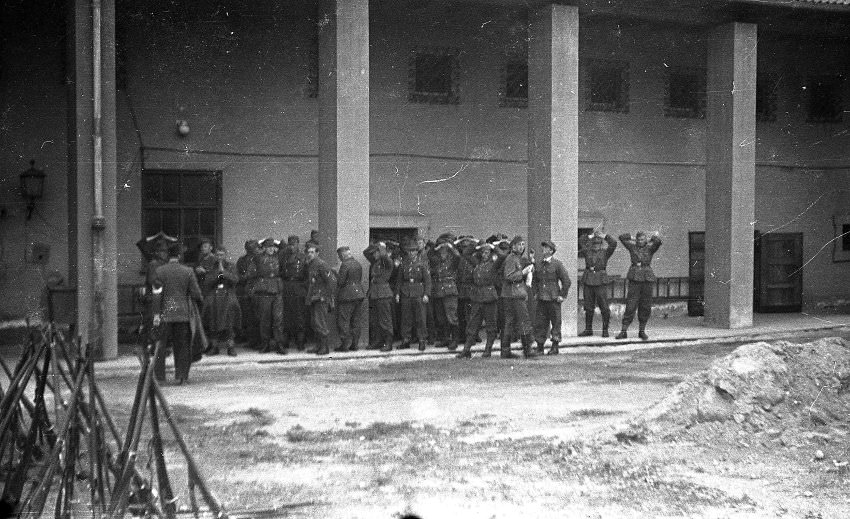 #17 The men in the background here have their hands raised. They are possibly the German camp guards who surrendered and turned in their weapons, seen in the left foreground of the picture.