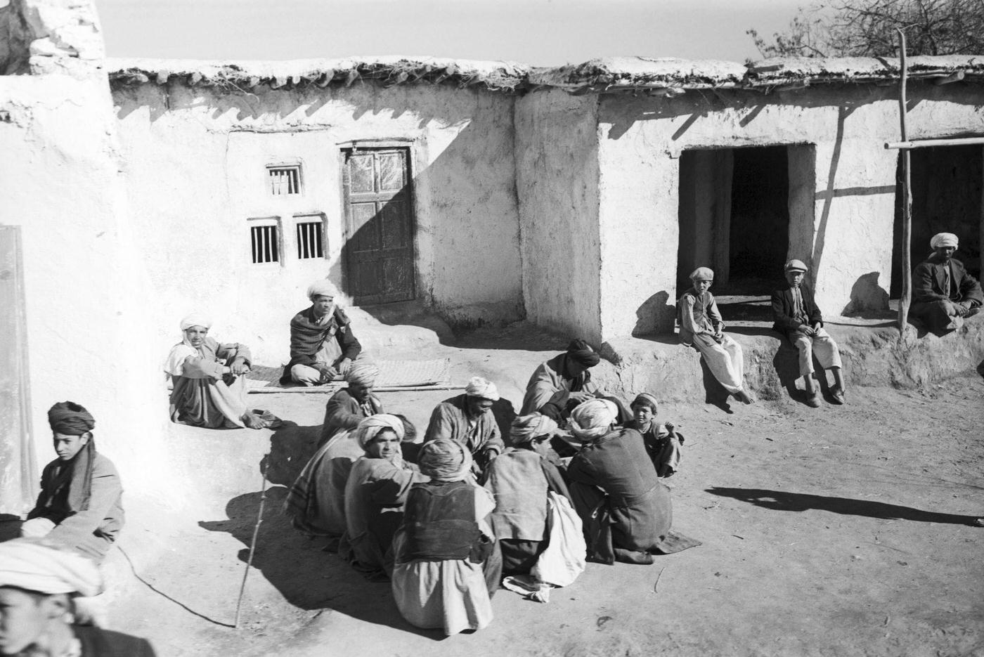 #48 People seated on the ground in front of their house on the road to Kabul, 1959