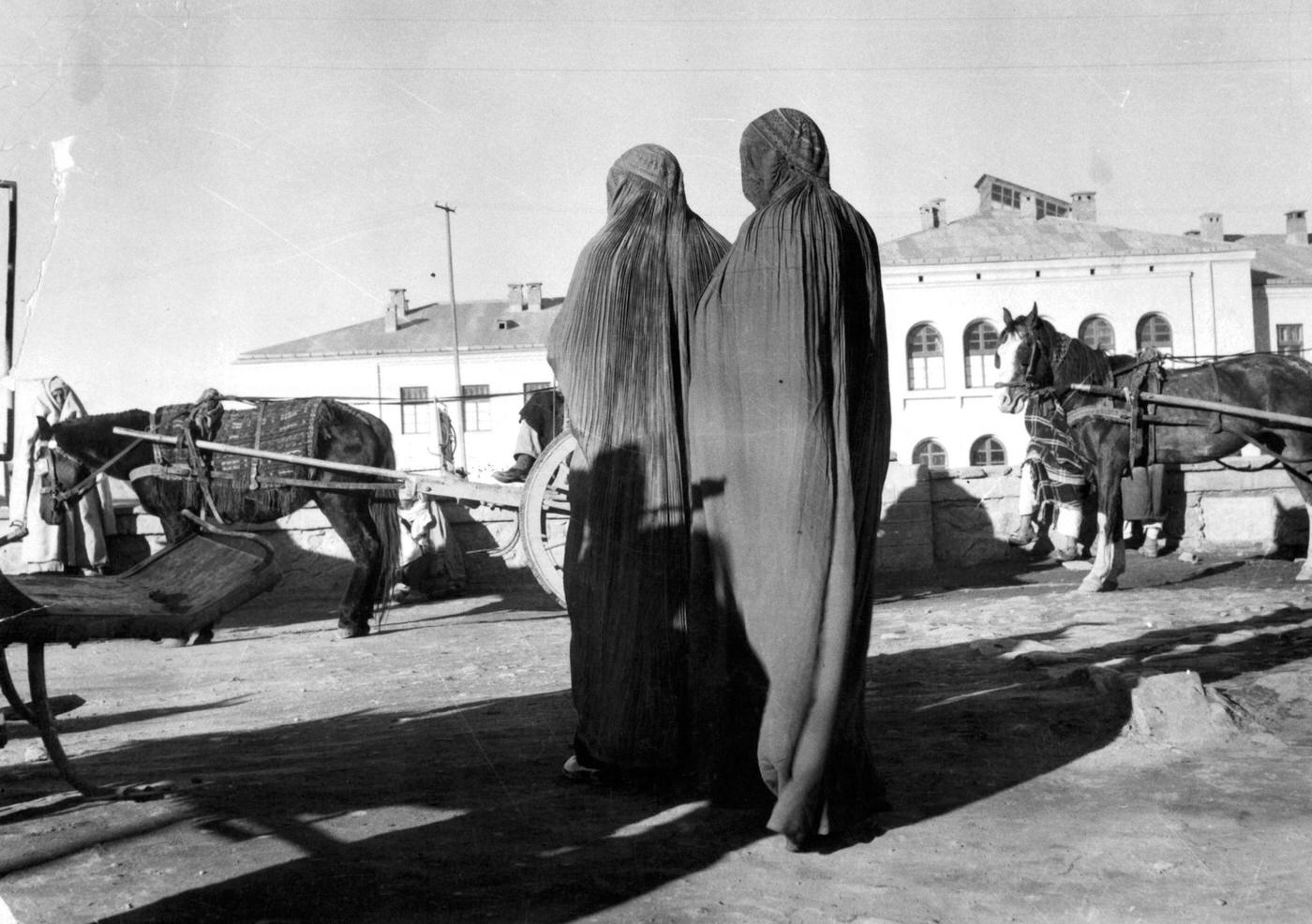 #52 Women in veils waiting for a “taxi” ponycart in a Kabul street, 1955.