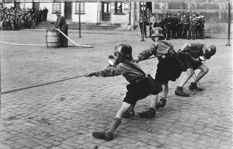 #4 Hitler Youth members playing tug of war while donning helmets and gas masks, 1933.