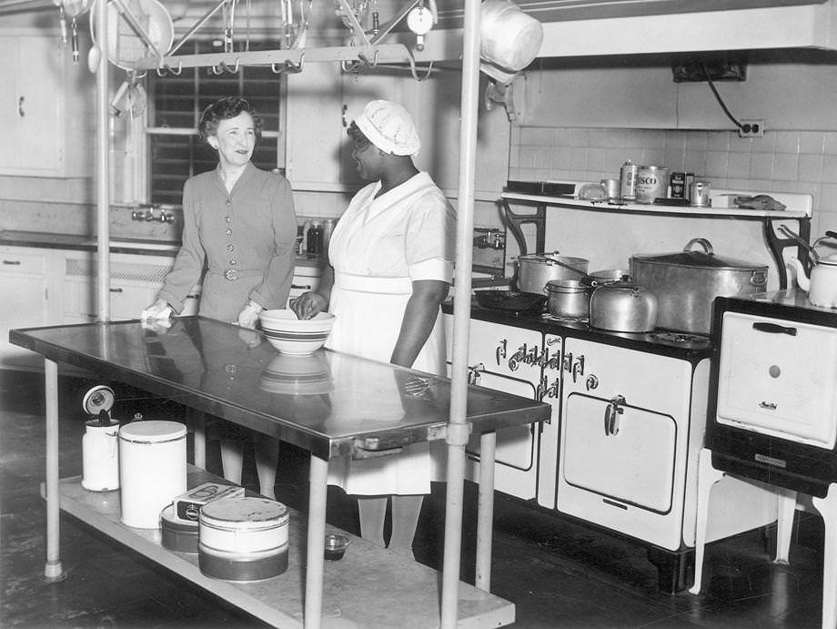#105 Mrs. Price looks on while Lucille, the mansion’s cook, mixes up something special in the kitchen, which has been completely renovated during the Price administration, 1942.