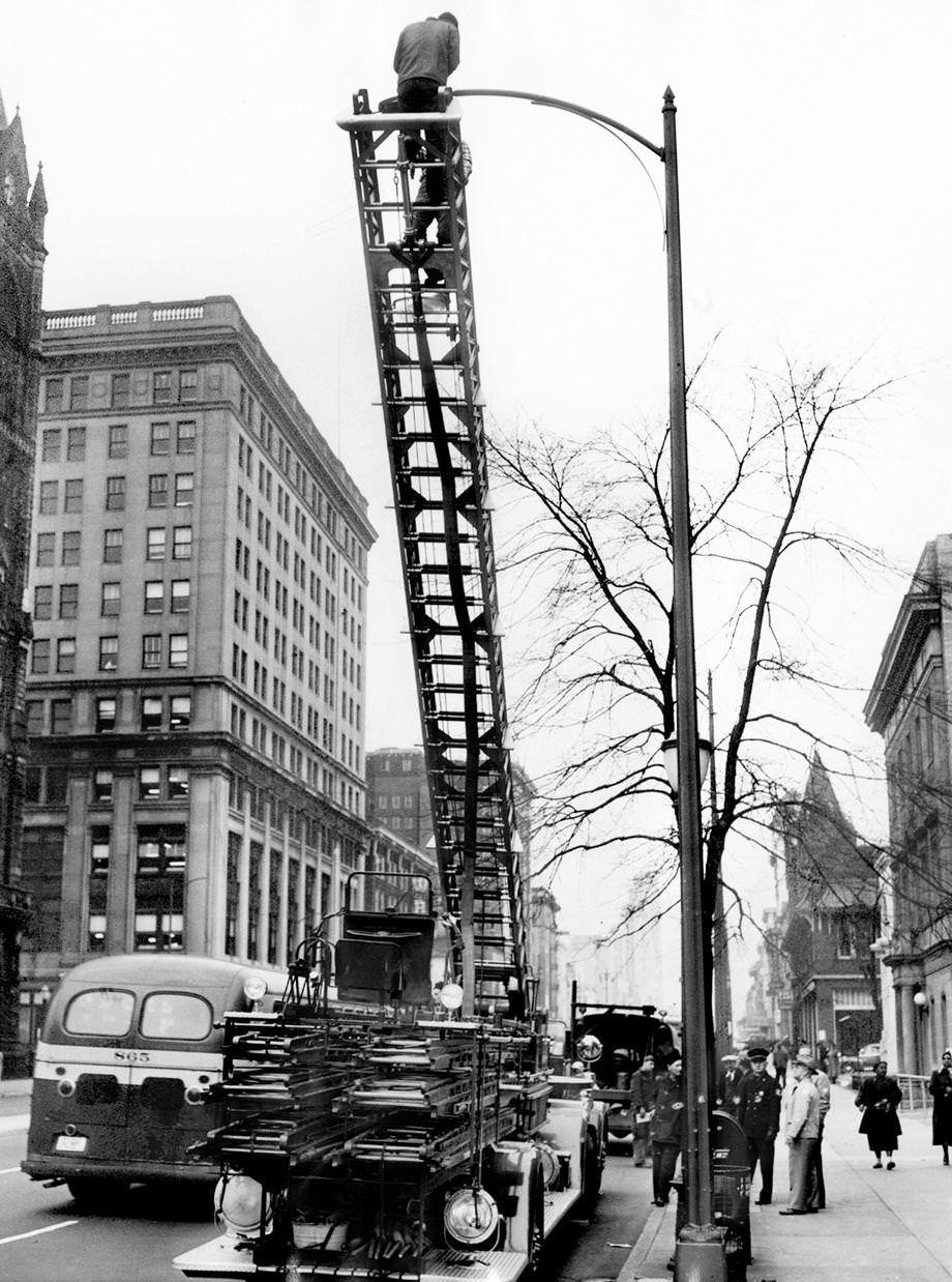 #69 Richmond Department of Utilities workers used a 65-foot hook-and-ladder fire truck to install new lights on Broad Street after attempts to secure other ladder facilities from private companies had failed, 1953.
