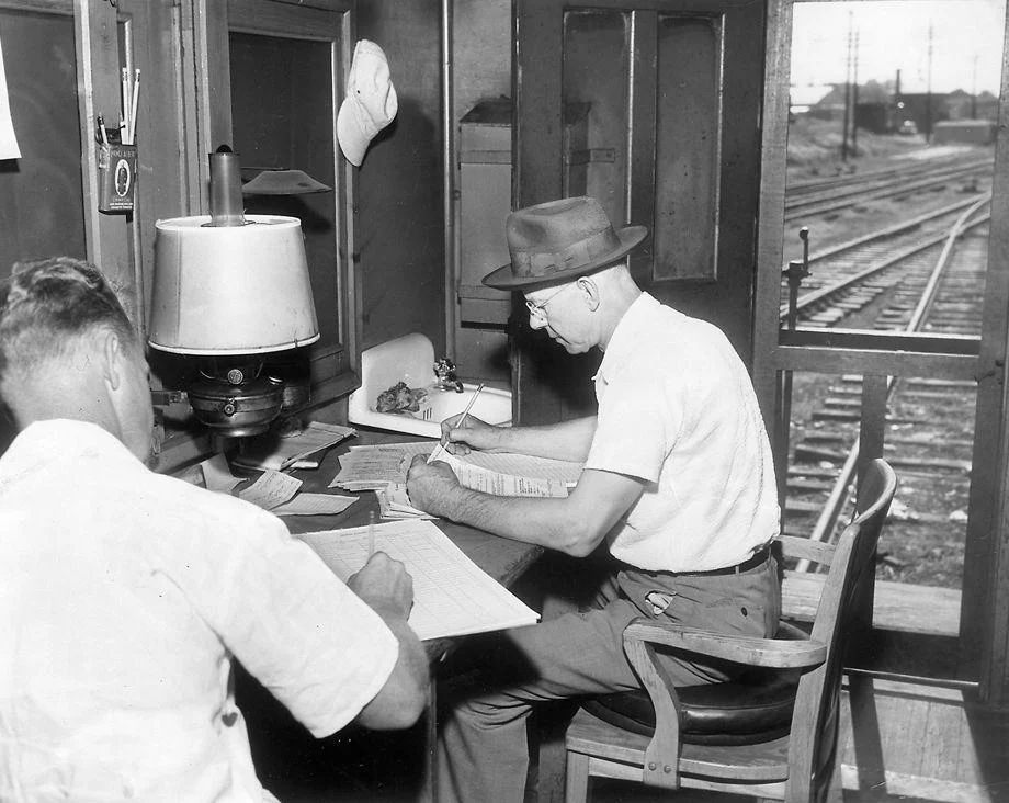 #81 Fredericksburg and Potomac Railroad conductor H.C. Rollins (right) and flagman C.H. Smith did pre-trip paperwork in a train caboose before a ride to Washington, 1953.