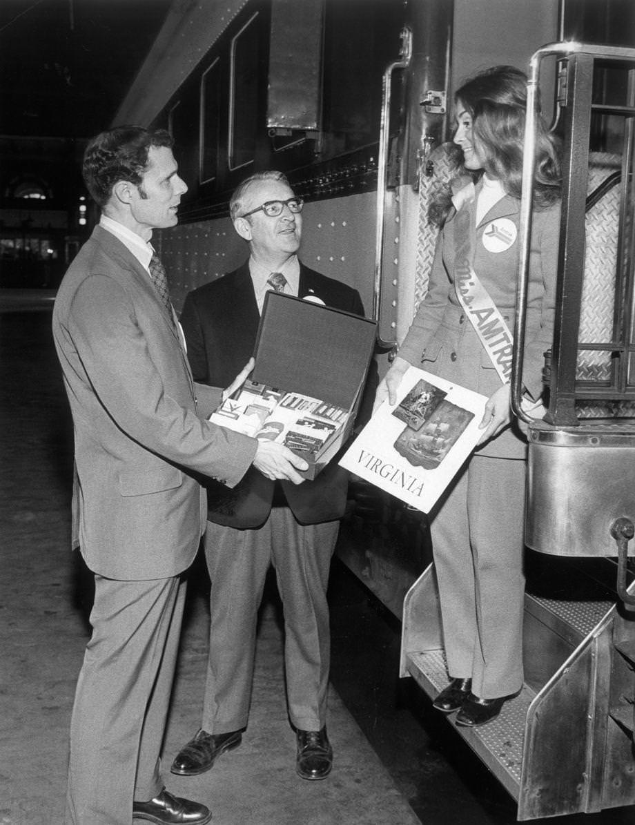 #146 As Amtrak consolidated passenger rail service in America, E.M.C. Quincy (left) of the Greater Richmond Chamber of Commerce presented a gift of Richmond tobacco products and a record about Virginia to Amtrak’s Teresa Cunningham at Main Street Station in downtown Richmond, 1971.