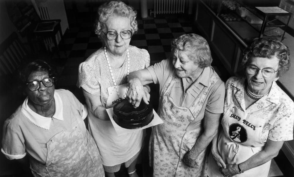 #18 Veterans at Sally Bell’s Kitchen in Richmond – Lucille Zimmerman (from left), Mary Newcomb, Dorothy Daniels and Anne Mulfinger – posed with one of the countless cakes they had prepared over decades of working together, 1990