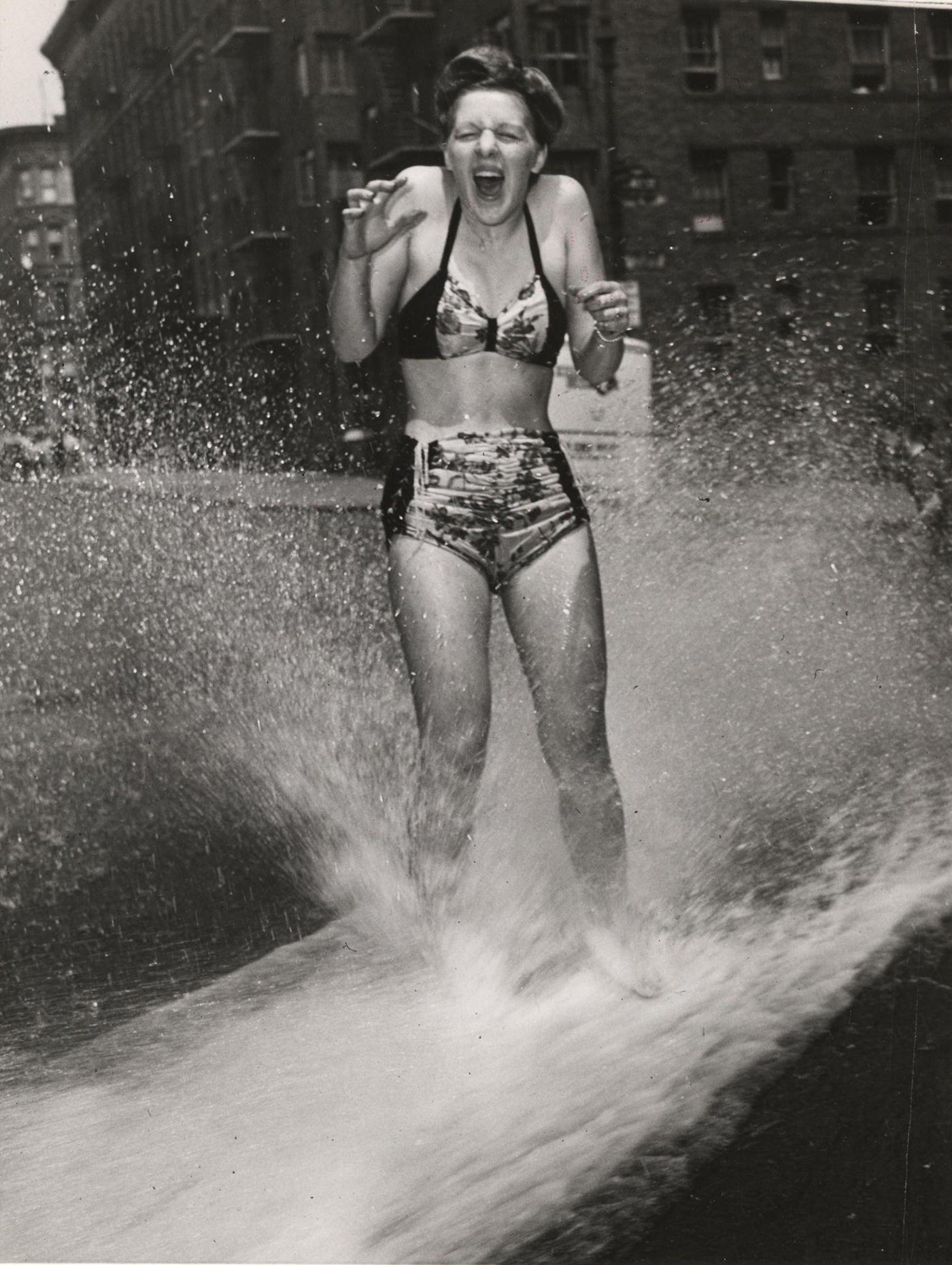 #1 Woman in a two-piece bathing suit cools down under a fire hydrant spray, 1930s