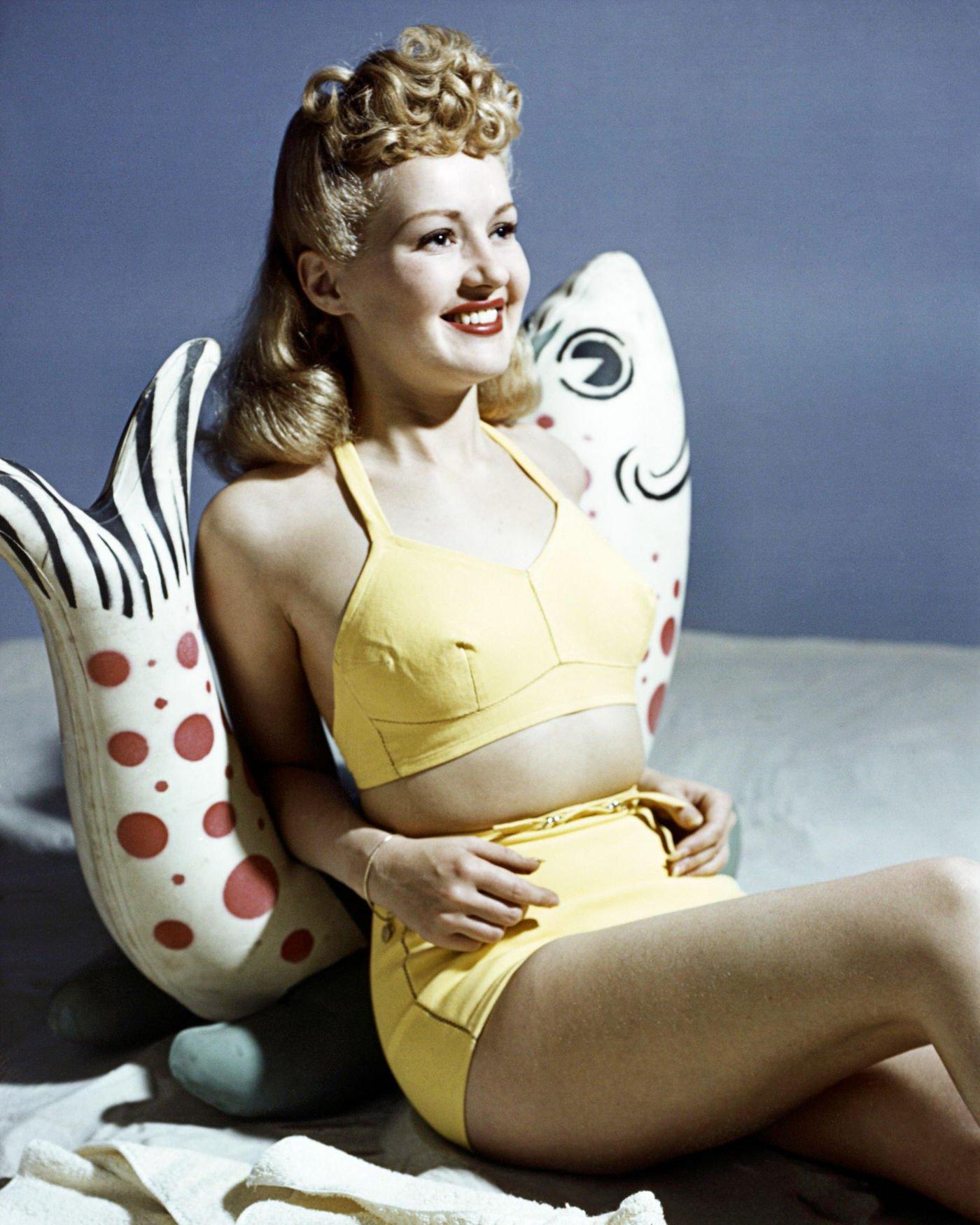 #3 Betty Grable, US actress, in a yellow bikini leaning against a fish ornament, 1940.