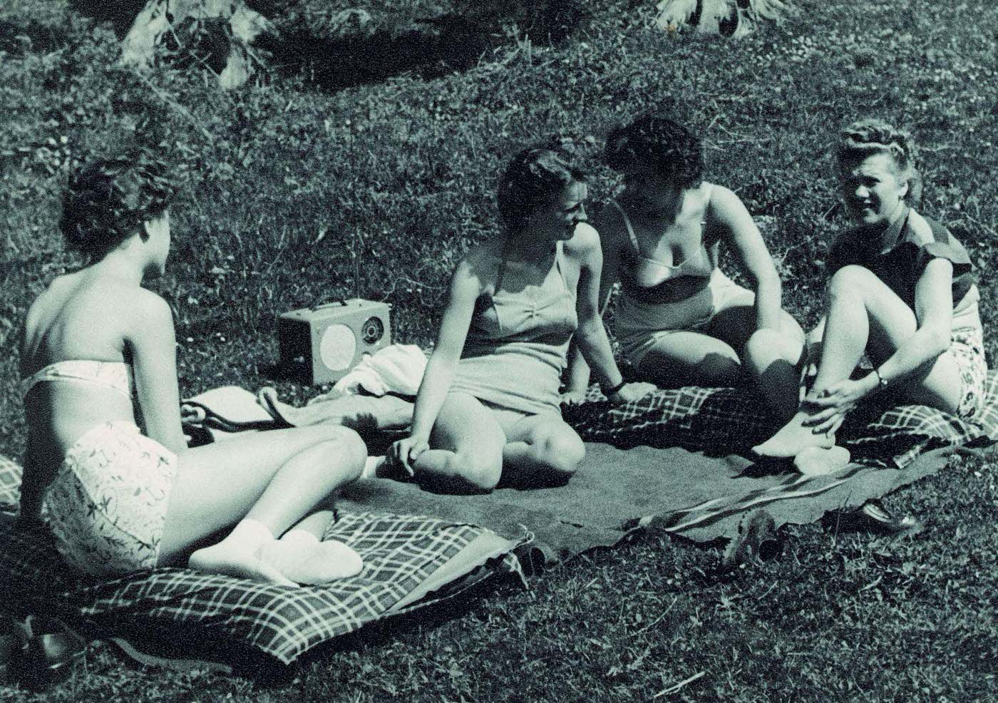 #53 Four girls sitting on a blanket in the grass wearing swimsuits and bikinis, Switzerland, 1948.