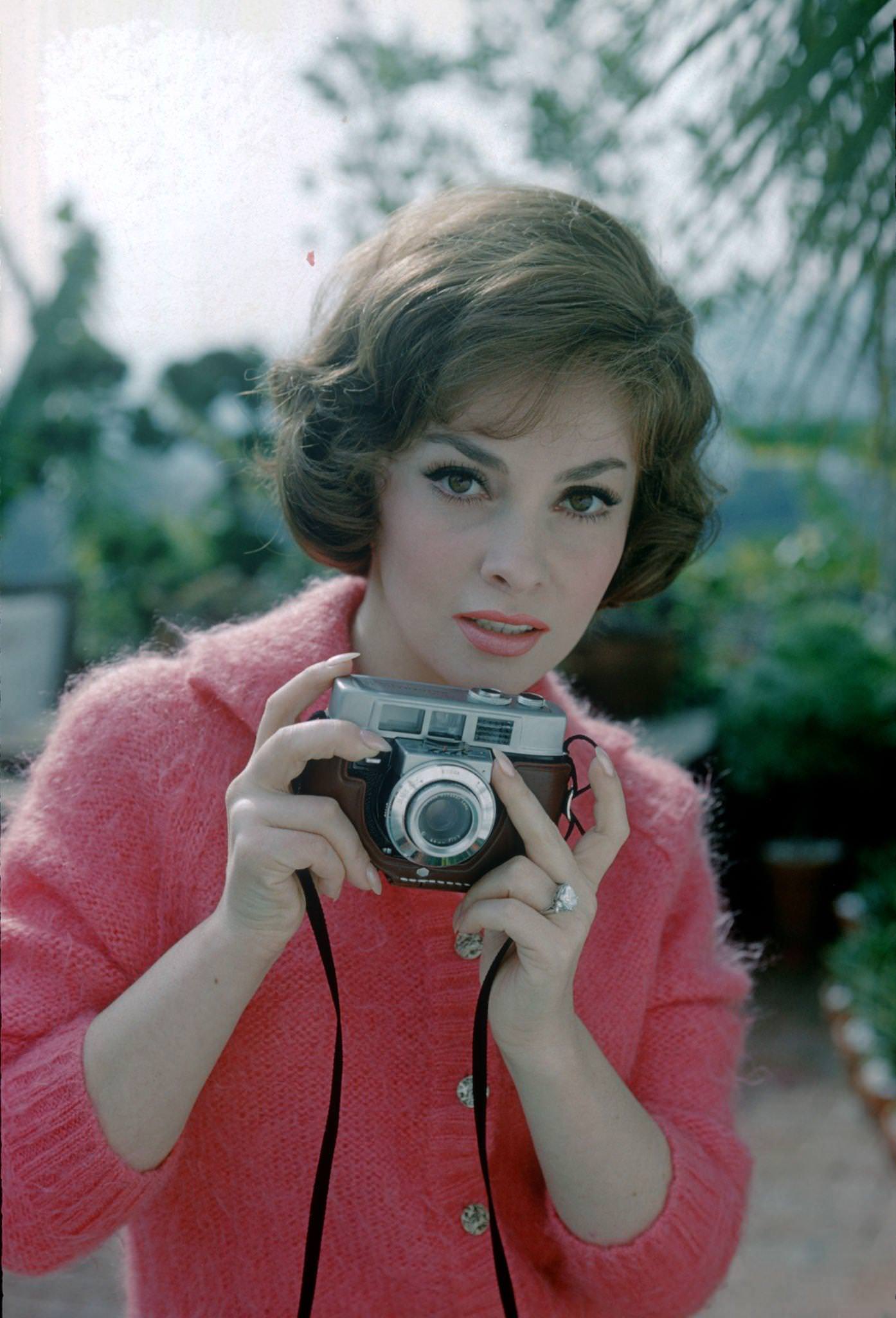 #100 Gina Lollobrigida poses with a camera in Portofino, Italy, 1960.
