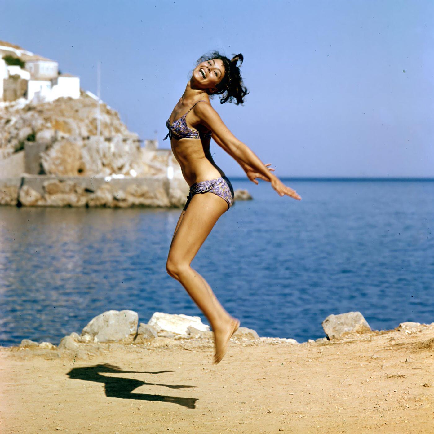 #68 Giorgia Moll happily jumping at the beach, filming ‘Island of Love,’ Greece, 1962